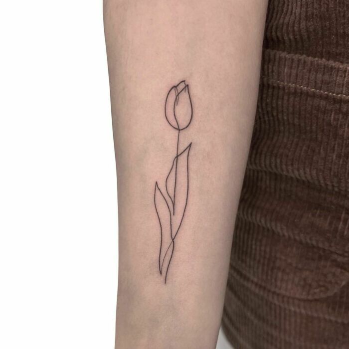 Single-line tattoo of a tulip on forearm, showcasing fine-line perfection.