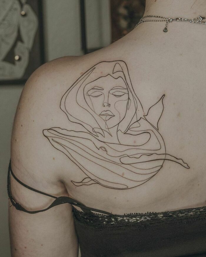 Single-line tattoo of a serene face intertwined with a whale on a person's back.