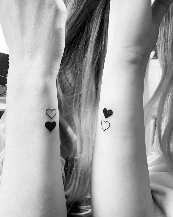 Matching heart tattoos on forearms symbolize friendship and bond.