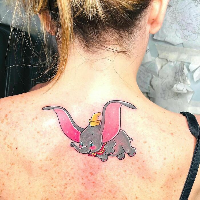 Cartoon tattoo of a flying elephant on a woman's back, featuring childhood favorite character design.