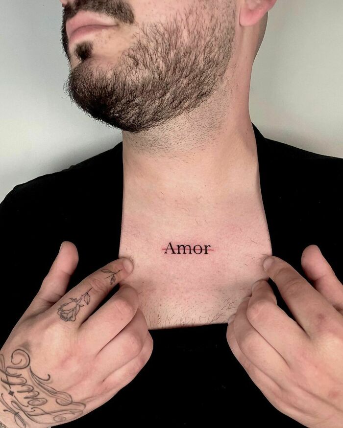 Chest tattoo with the word "Amor," featuring creative ink design on a person with a beard and hand tattoos.