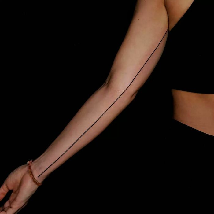 Minimalist single-line tattoo stretching down an arm against a black background.
