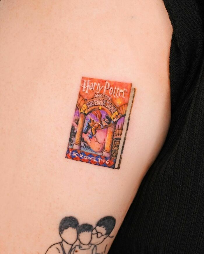 Harry Potter tattoo of the Sorcerer's Stone book cover on upper arm, showcasing vibrant colors and intricate design.