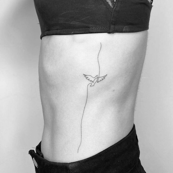 Fine-line tattoo of a bird on a person's side, minimalist single-line design.
