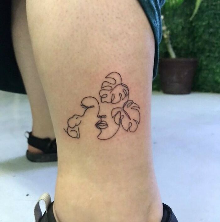 Minimalist line tattoo featuring abstract face with leaves on a person's leg.