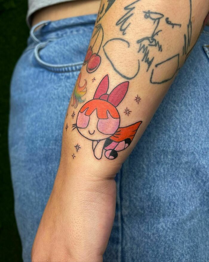 Cartoon tattoo of a red-haired character from an animated show on a forearm, surrounded by other small designs.