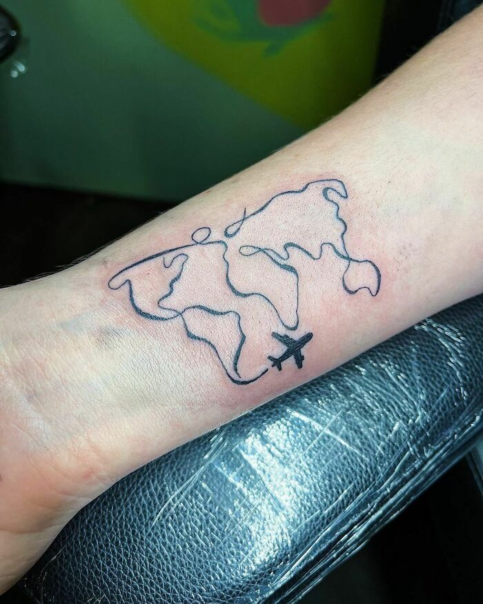 Minimalism line tattoo of world map with airplane on forearm.