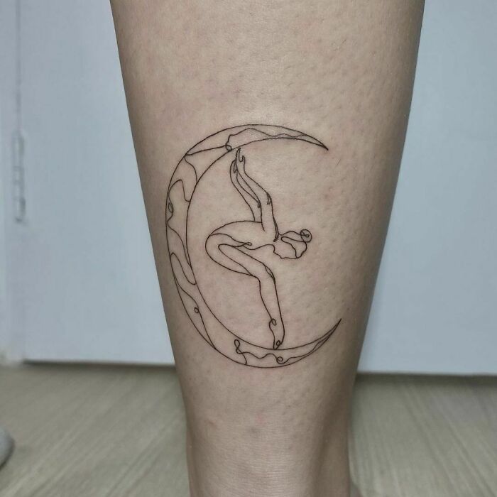 Single-line tattoo of a ballerina gracefully posed within a crescent moon on a person's leg.