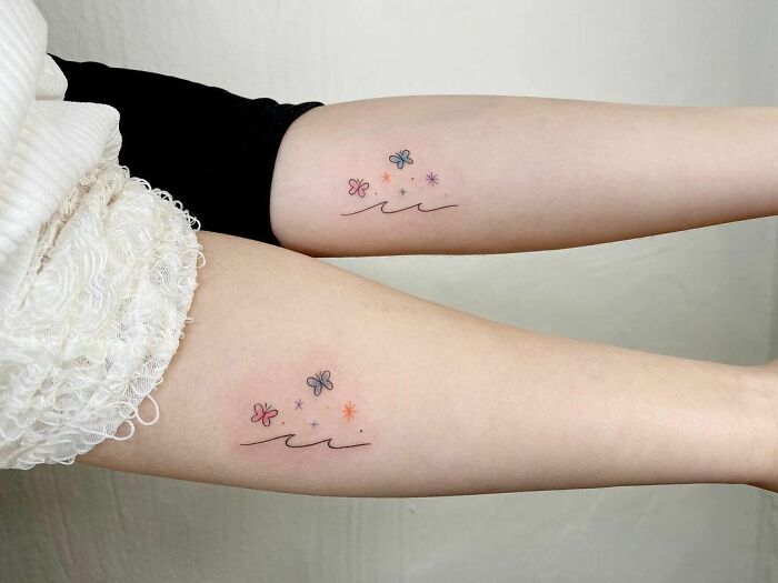 Two forearms with matching BFF tattoos of butterflies and stars in minimalist style.