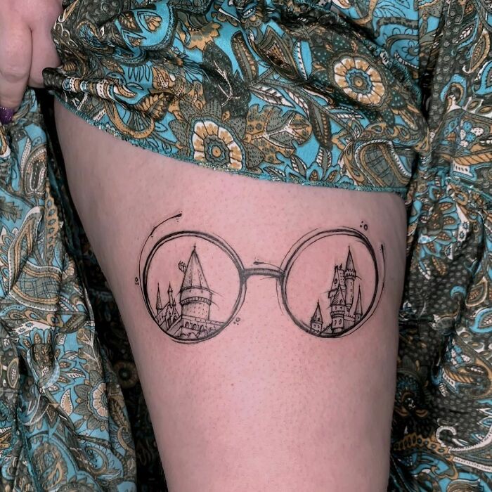 Harry Potter tattoo of glasses with castle design on a thigh, featuring intricate linework.