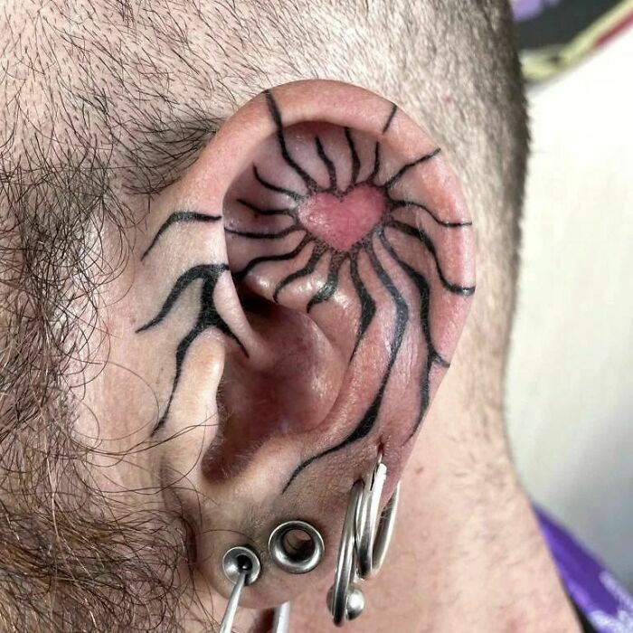 Unique ear tattoo with a heart and radiating lines, featuring ear piercings.