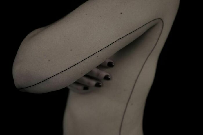 Fine-line single-line tattoo on an arm, showcasing minimalist art in black ink against a dark background.