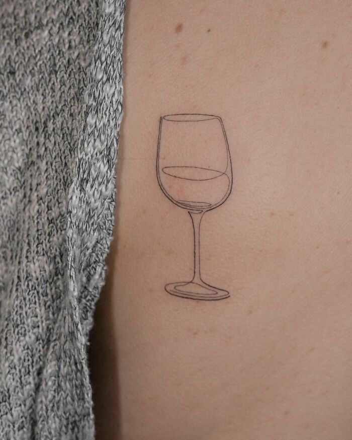 Single-line tattoo of a wine glass on skin.