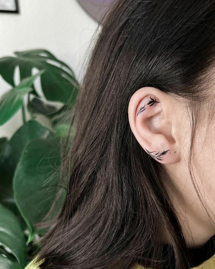 Ear tattoo with a delicate leaf design, blending subtly with dark hair.