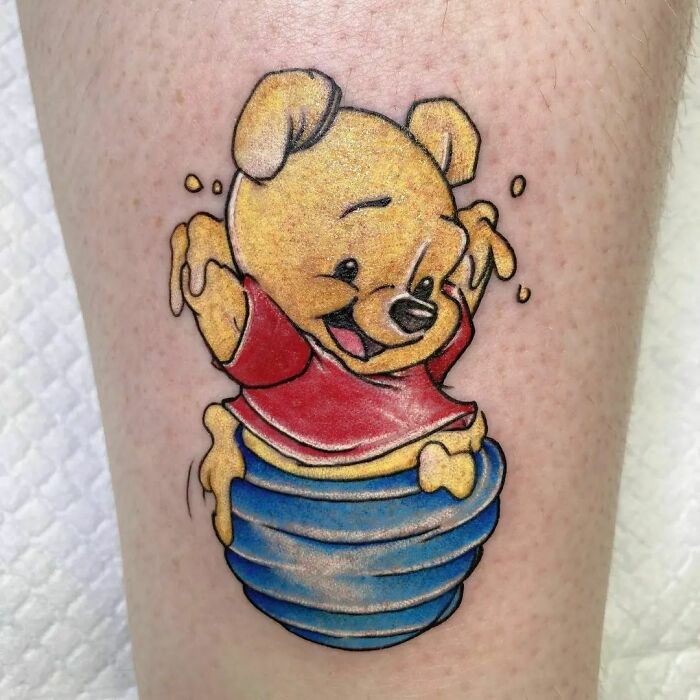 Cartoon tattoo of a smiling bear in a red shirt sitting in a honey pot, celebrating childhood favorites.