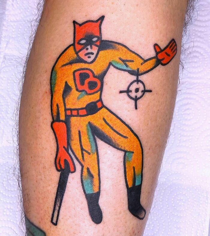 Marvel tattoo depicting a superhero costume, with an orange and red design, featuring a mask and gloves.