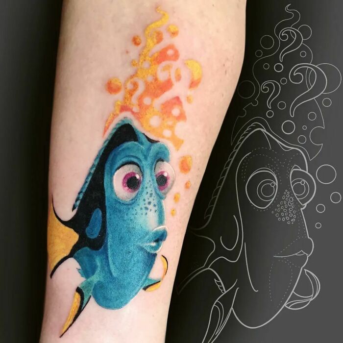 Colorful cartoon tattoo of a blue fish Dory character with bubbles on an arm, showcasing vibrant design work.