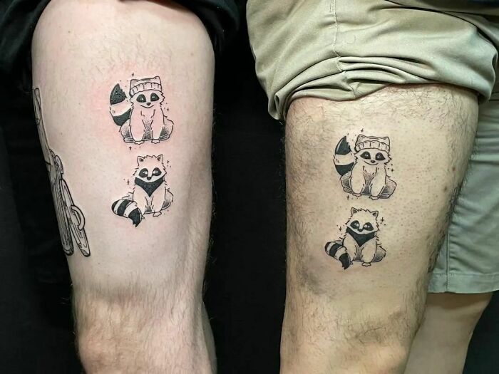 Matching raccoon friend tattoos on two people's thighs, celebrating friendship.