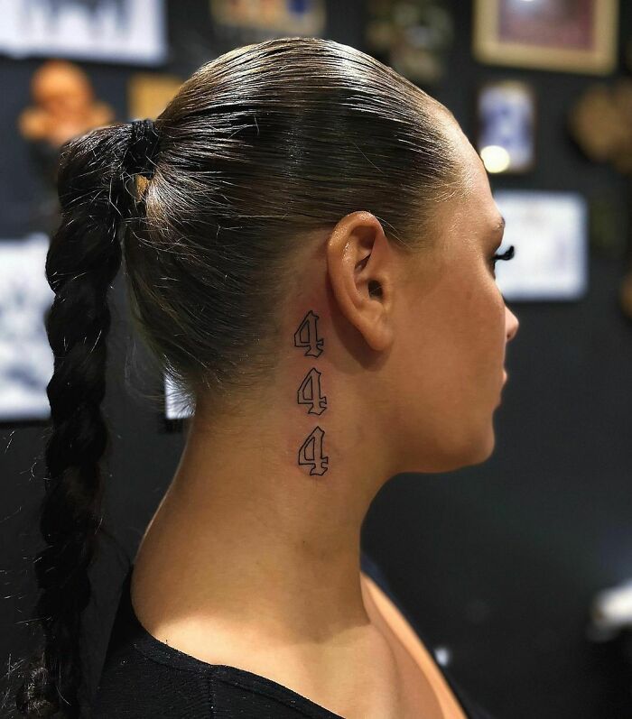 Woman with a sleek ponytail displaying a numeric tattoo behind her ear.