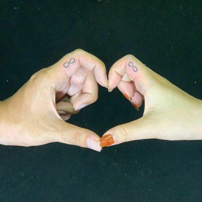 Two hands with matching infinity symbol tattoos, forming a heart to symbolize brother and sister bond.
