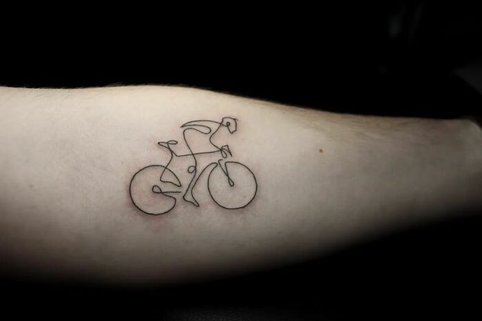 Minimalist single-line tattoo of a cyclist on an arm.