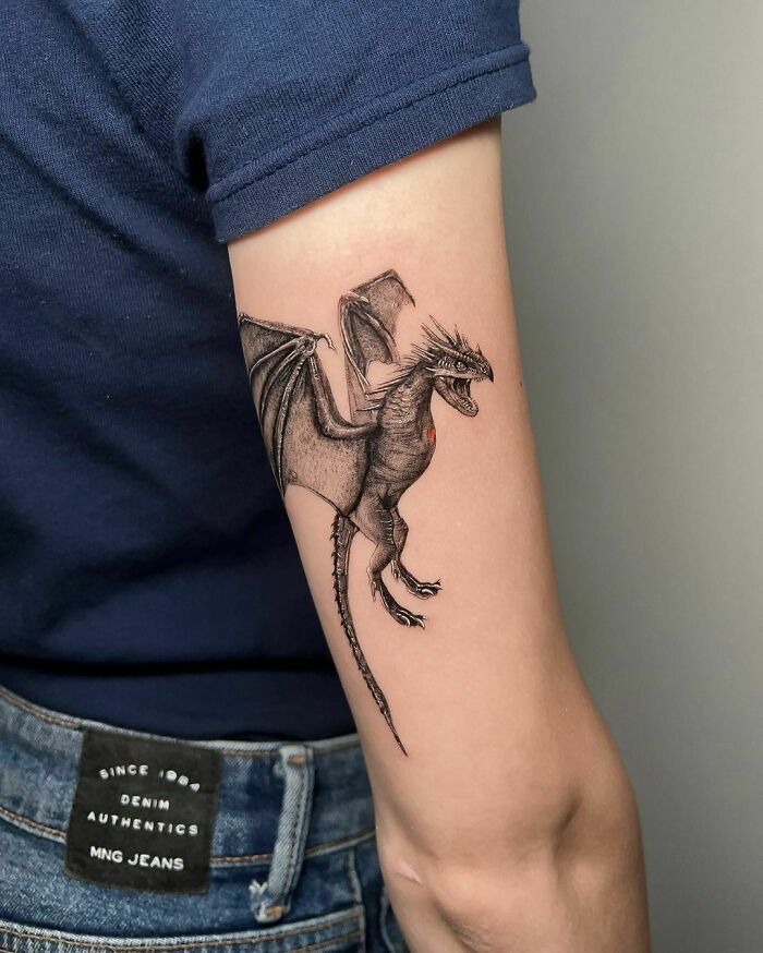Dragon tattoo on arm for Harry Potter fans, wearing a blue shirt and jeans.