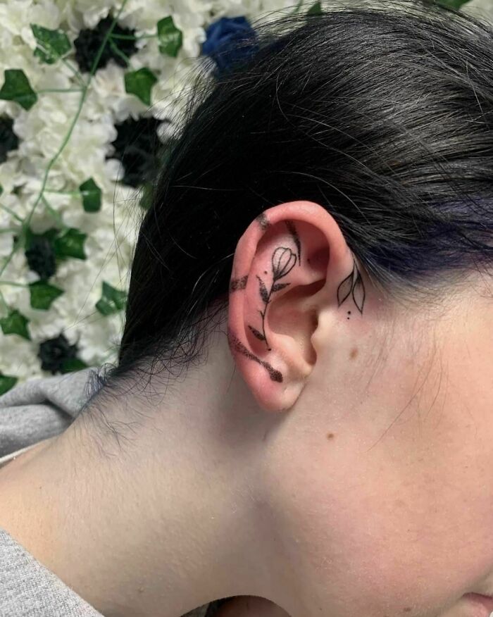 Delicate floral ear tattoo with leaves and petals behind a woman's ear.