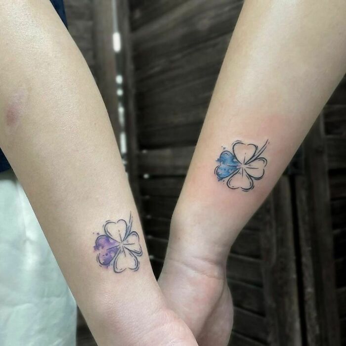 Matching BFF tattoos of four-leaf clovers on forearms with watercolor accents.
