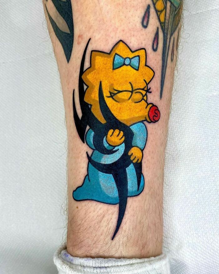 Cartoon tattoo of a baby character Maggie Simpson in a blue outfit with a pacifier on a person's leg.