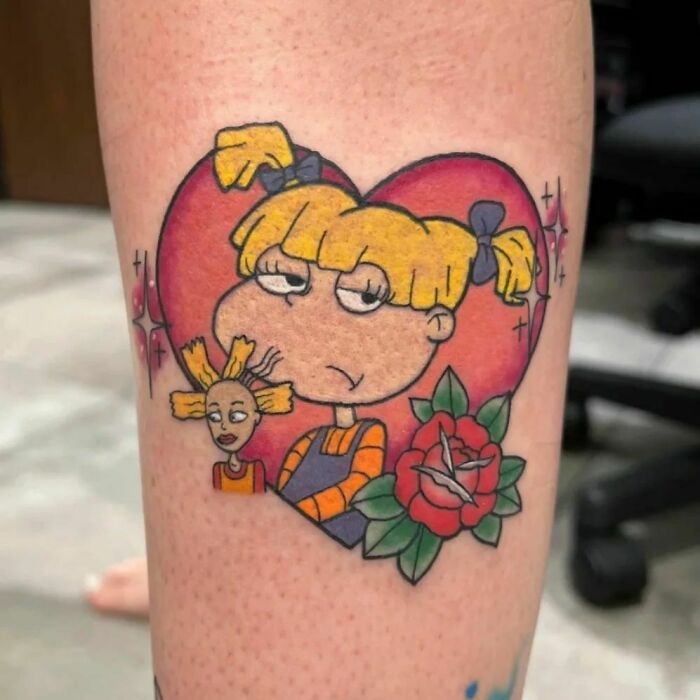 Cartoon tattoo featuring a character with blonde hair, set within a heart and rose design, showcasing nostalgic art style.