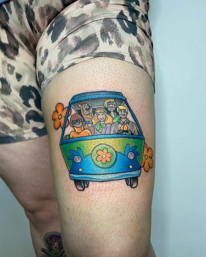 Cartoon tattoo of a childhood favorite on the thigh, featuring characters riding in a colorful van.