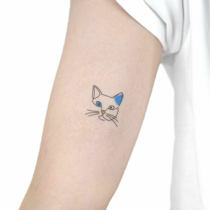 Single-line cat tattoo with blue eyes on a person's arm, showcasing minimalist design.