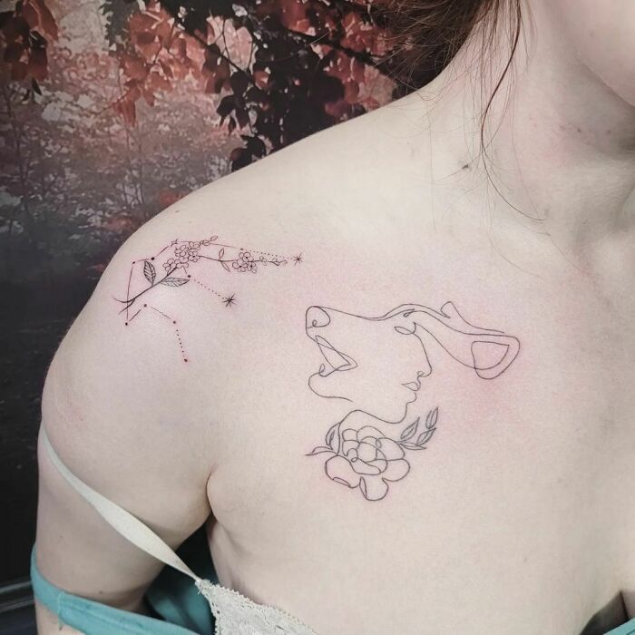 Fine-line single-line tattoos on a person's shoulder featuring a face, floral elements, and constellations.