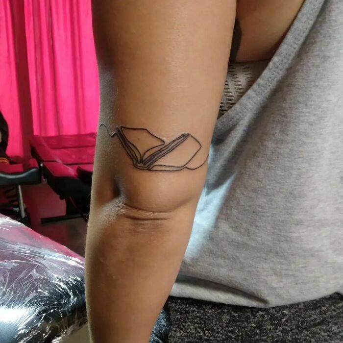 Single-line tattoo of an open book on an arm, showcasing fine-line artistry.