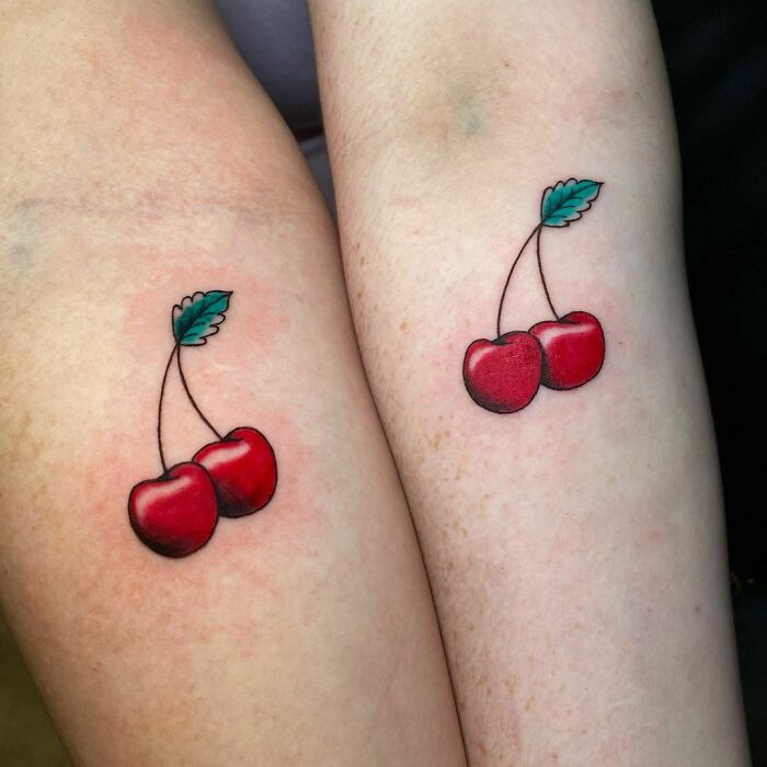 Matching cherry tattoos symbolizing friendship on two arms.