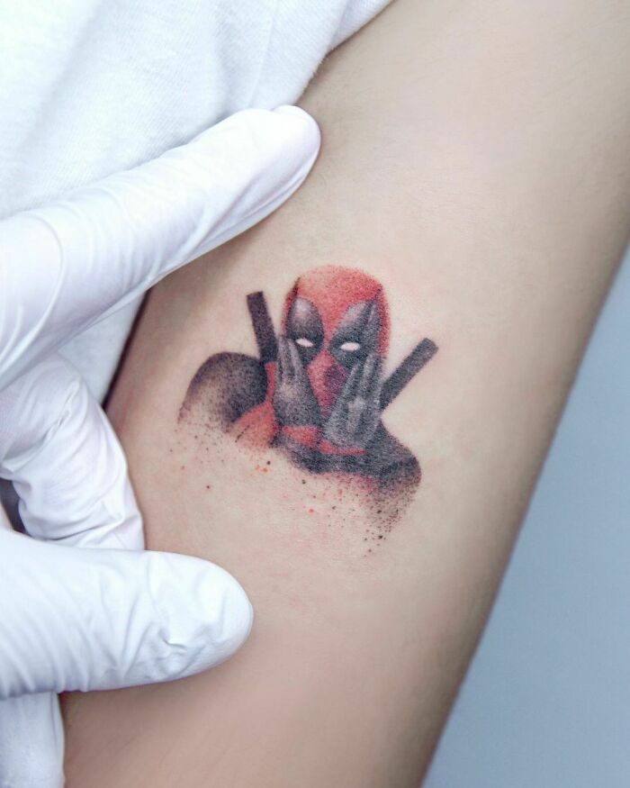 Tattoo of a Marvel character Deadpool with hands on face, featured on an arm, showcasing detailed artistry.