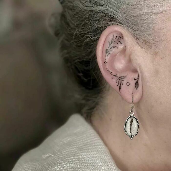 Decorative ear tattoo with floral design behind ear, paired with a seashell earring.