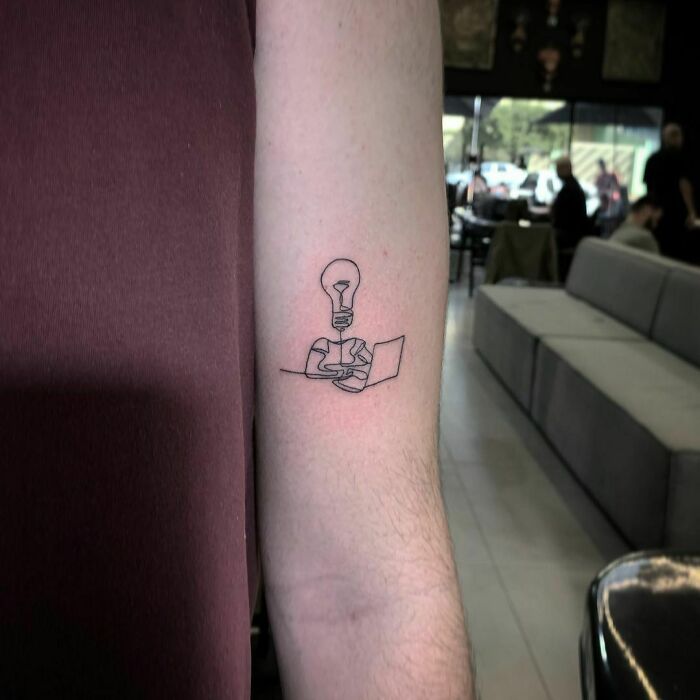 Single-line tattoo of a light bulb and puzzle on an arm, showcasing fine-line perfection.