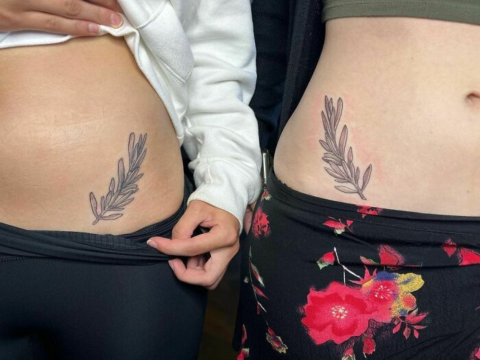 Matching BFF tattoos of leafy branches on hips, symbolizing friendship and unity.