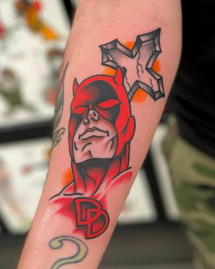 Marvel tattoo featuring a red superhero design on a forearm, with bold lines and a dynamic pose.