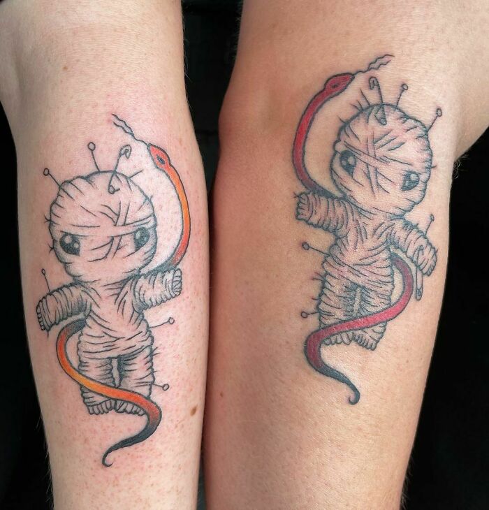 Matching best friend tattoos of a cute, wrapped creature with a red and orange snake around it on two arms.
