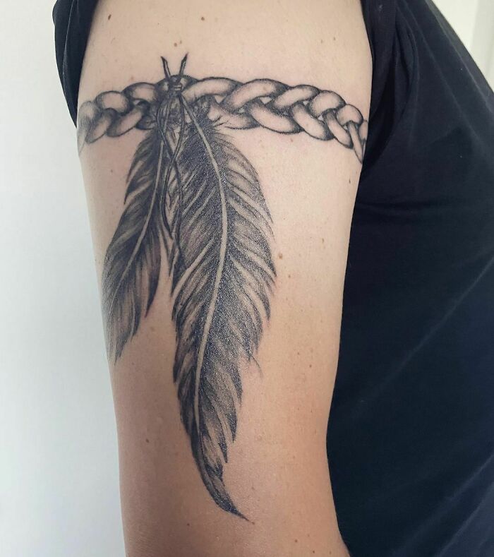 Armband tattoo with braided design and feathers on upper arm.