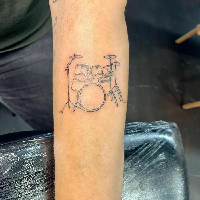 Fine-line single-line tattoo of a drum set on an arm, showcasing minimalist design.