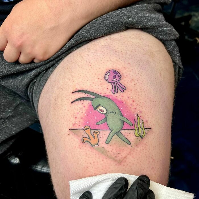 Cartoon tattoo on thigh featuring sea creature Plankton and coral in vibrant colors.