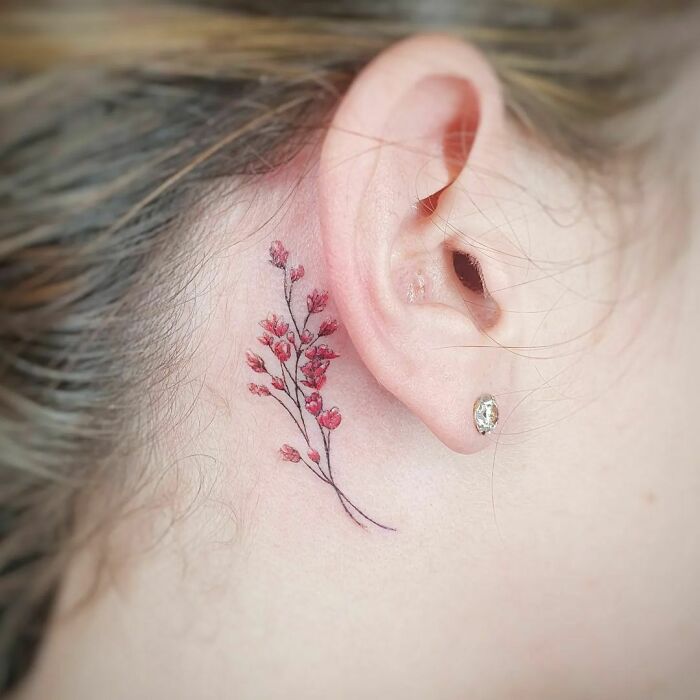 Floral ear tattoo with delicate pink blossoms behind the ear.