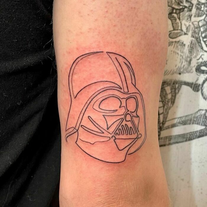 Minimalist line tattoo of a helmet design on the arm.