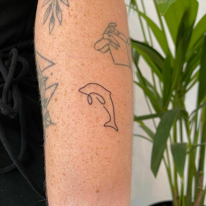 Fine-line dolphin tattoo in a single line on forearm, showcasing minimalist tattoo artistry.