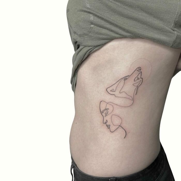 Minimalist line tattoo of a face and a howling wolf on side of a person's torso.