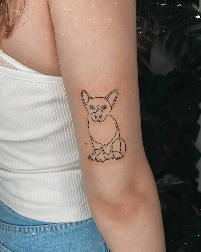 Minimalist line tattoo of a dog on a person's arm in a simple design.