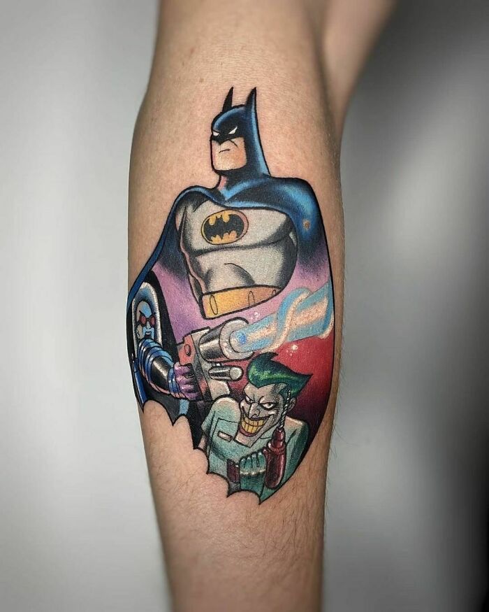 Cartoon tattoo featuring a superhero Batman and villain Joker in vibrant colors on someone's forearm.